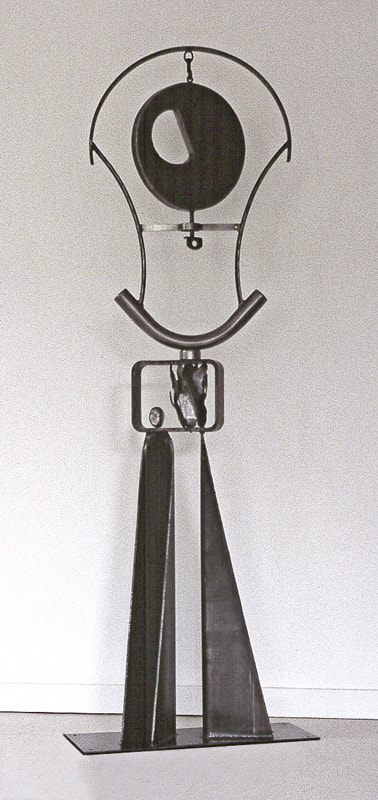 Dark metallic vertical abstract sculpture with two supports, linear elements, a circle and a small aluminum head with male and female faces.