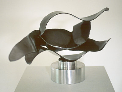 A dark steel abstract scultpure of flame-liek or water-like wavy shapes above a smooth, shiny aluminum base element.