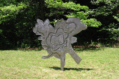 A steel footprint made from a maple tree. It is vertical and stands only on one point. It is wind kinetic, apparently abstract, taller and wider than a person, but also flat.