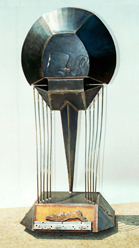 Dark steel sculpture reminiscent of a horseshoe crab suspended vertically over a base with curved steel rod to suggest water. There is a small door in front.