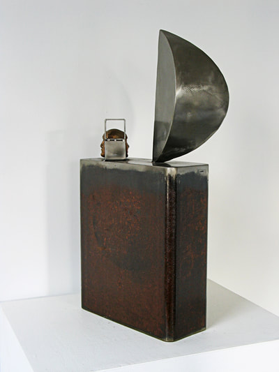 A rectangular steel sculpture topped by a wedge shape standing on end and a two sided face cast in bronze.