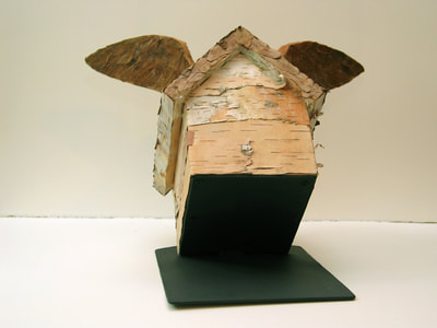 A little wooden winged house  covered with birch bark, leaves and maple seeds. It is tipped up over its black steel base as if about to take off in flight.